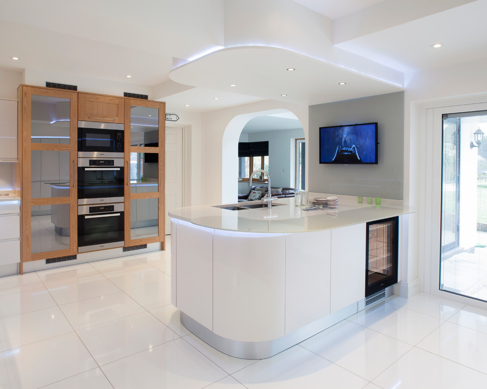 This is an example of a mid-sized contemporary u-shaped eat-in kitchen in Other with a double-bowl sink, flat-panel cabinets, white cabinets, recycled glass benchtops, white splashback, glass sheet splashback, white appliances, ceramic floors and with island.