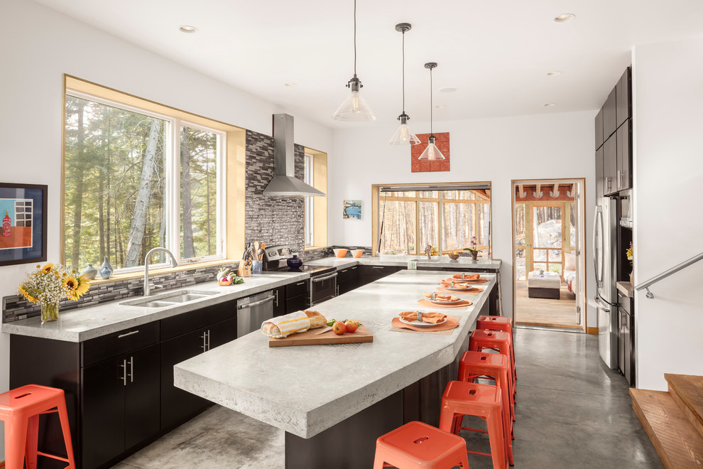 Photo of a country l-shaped open plan kitchen in Portland Maine with a double-bowl sink, flat-panel cabinets, black cabinets, concrete benchtops, multi-coloured splashback, glass tile splashback, stainless steel appliances, concrete floors, with island, grey floor and grey benchtop.