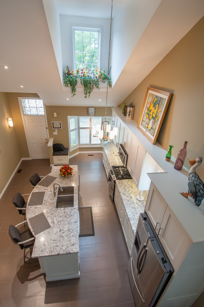 Inspiration for a mid-sized transitional galley ceramic tile eat-in kitchen remodel in Toronto with a double-bowl sink, shaker cabinets, white cabinets, granite countertops, beige backsplash, stone tile backsplash, stainless steel appliances and an island