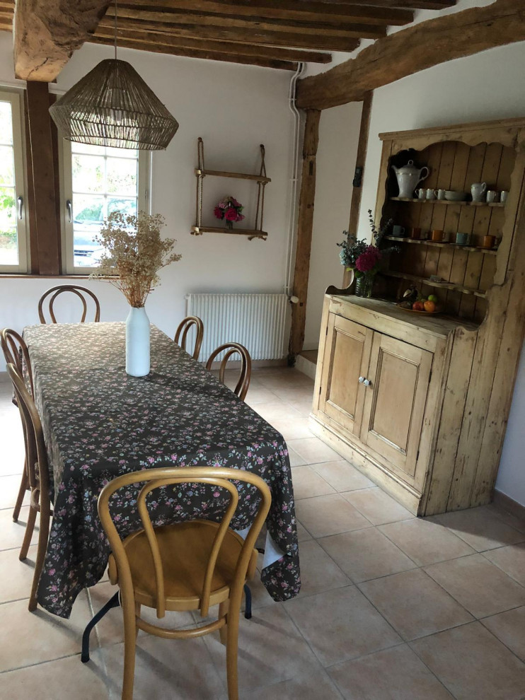 Cette photo montre une salle à manger ouverte sur le salon nature de taille moyenne avec un mur blanc, un sol beige et poutres apparentes.