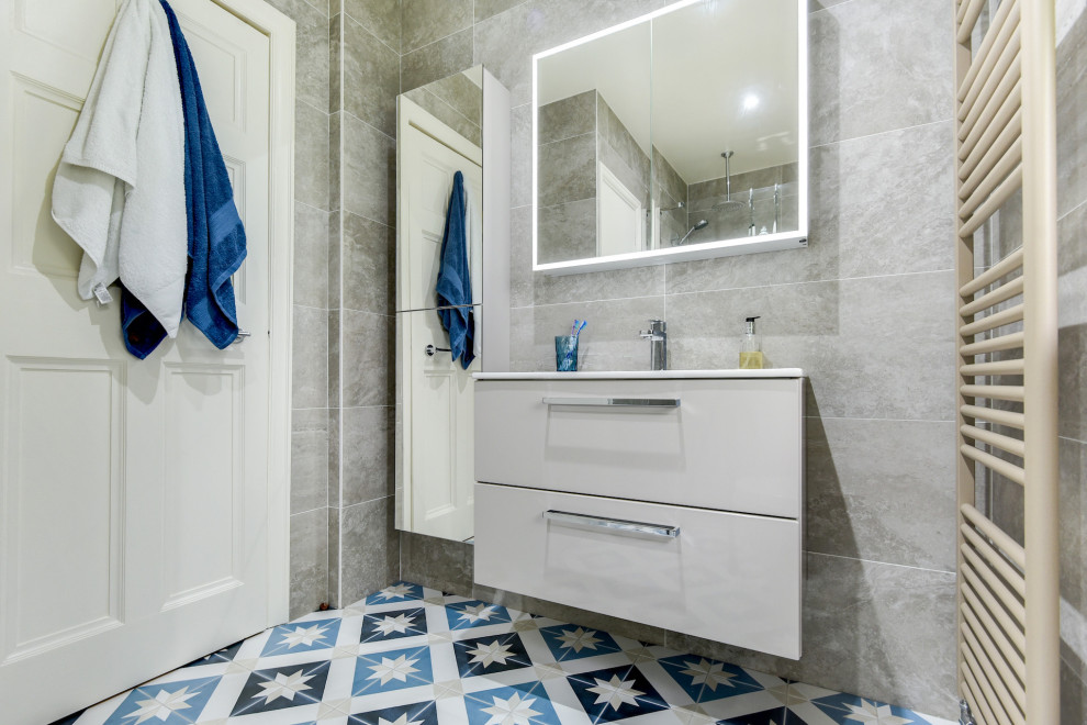 Small contemporary grey and teal ensuite bathroom in Sussex with flat-panel cabinets, beige cabinets, a walk-in shower, a two-piece toilet, beige tiles, ceramic tiles, ceramic flooring, a built-in sink, blue floors, an open shower, feature lighting, a single sink and a floating vanity unit.
