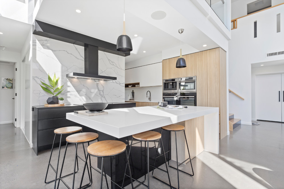 This is an example of a large contemporary open plan kitchen in Sunshine Coast with flat-panel cabinets, quartz benchtops, white splashback, marble splashback, stainless steel appliances, concrete floors, with island and grey floor.