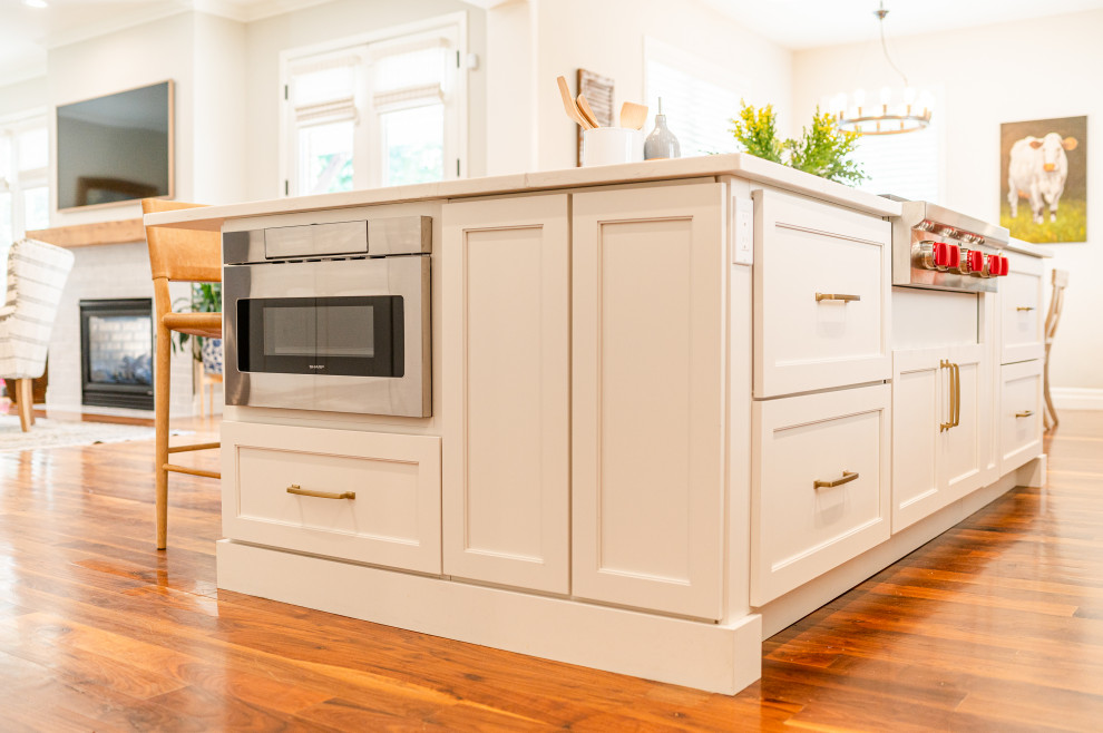 Inspiration for a large transitional l-shaped dark wood floor and brown floor open concept kitchen remodel in Denver with a farmhouse sink, shaker cabinets, beige cabinets, quartz countertops, beige backsplash, ceramic backsplash, stainless steel appliances, an island and white countertops