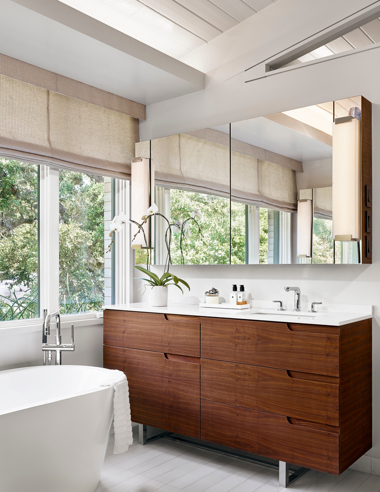 Inspiration for a mid-sized contemporary master bathroom in Austin with a freestanding tub, white walls, ceramic floors, an undermount sink, solid surface benchtops, medium wood cabinets, white benchtops and flat-panel cabinets.