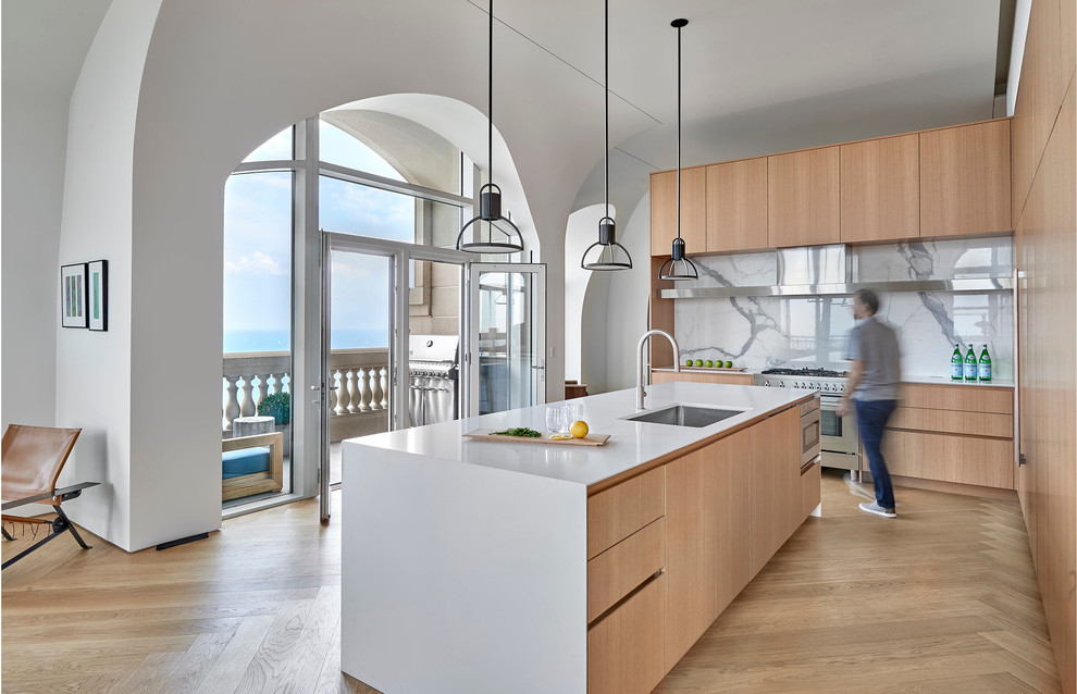 Photo of a contemporary kitchen in Chicago with an undermount sink, flat-panel cabinets, light wood cabinets, white splashback, stone slab splashback, stainless steel appliances, light hardwood floors, with island and white benchtop.