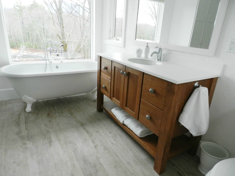 Photo of a large country master bathroom in New York with shaker cabinets, medium wood cabinets, a claw-foot tub, a curbless shower, a two-piece toilet, white tile, white walls, vinyl floors, an integrated sink, solid surface benchtops, grey floor and a hinged shower door.