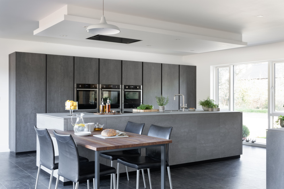 Photo of a large modern grey and black kitchen/diner in Oxfordshire with a double-bowl sink, flat-panel cabinets, grey cabinets, integrated appliances, ceramic flooring, an island and black floors.