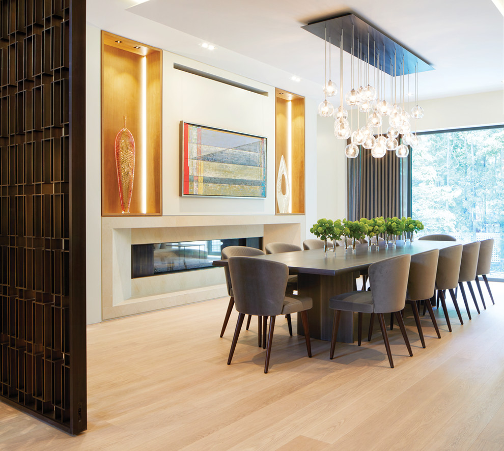 This is an example of a contemporary dining room in Toronto with white walls, light hardwood floors, a ribbon fireplace and beige floor.