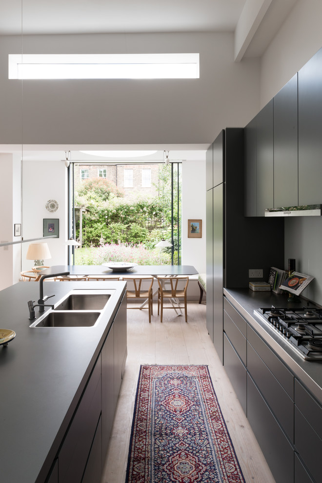 Inspiration for a mid-sized contemporary u-shaped open plan kitchen in London with an integrated sink, flat-panel cabinets, grey cabinets, solid surface benchtops, blue splashback, glass sheet splashback, stainless steel appliances, light hardwood floors, with island and beige floor.