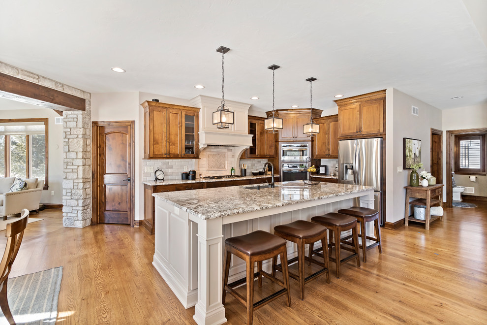 Open concept kitchen - large rustic l-shaped medium tone wood floor and brown floor open concept kitchen idea in Charleston with an undermount sink, medium tone wood cabinets, granite countertops, beige backsplash, stainless steel appliances, multicolored countertops, shaker cabinets and an island
