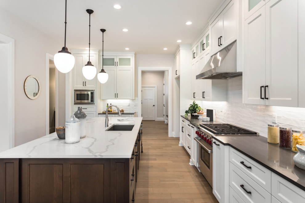 Enclosed kitchen - huge transitional l-shaped medium tone wood floor and beige floor enclosed kitchen idea in Houston with an undermount sink, shaker cabinets, white cabinets, white backsplash, stainless steel appliances, an island and black countertops