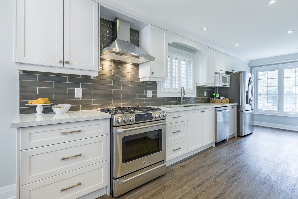 Design ideas for a transitional eat-in kitchen in Toronto with an undermount sink, shaker cabinets, white cabinets, quartzite benchtops, brown splashback, glass tile splashback, stainless steel appliances, vinyl floors, with island and brown floor.