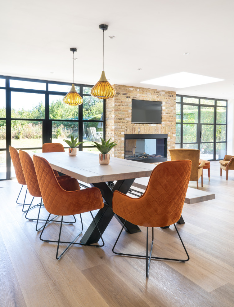 Contemporary open plan dining in Hertfordshire with white walls, medium hardwood floors, a ribbon fireplace, a brick fireplace surround and brown floor.