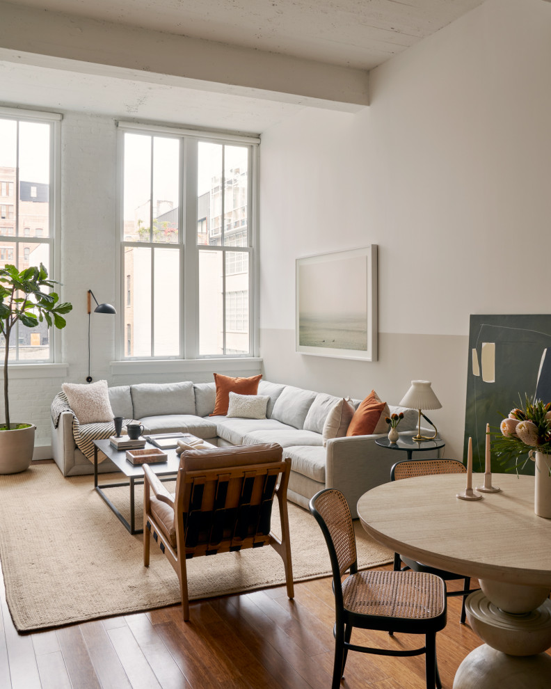 Inspiration for a mid-sized contemporary loft-style living room in New York with beige walls, medium hardwood floors, no fireplace, a wall-mounted tv, brown floor, exposed beam and brick walls.