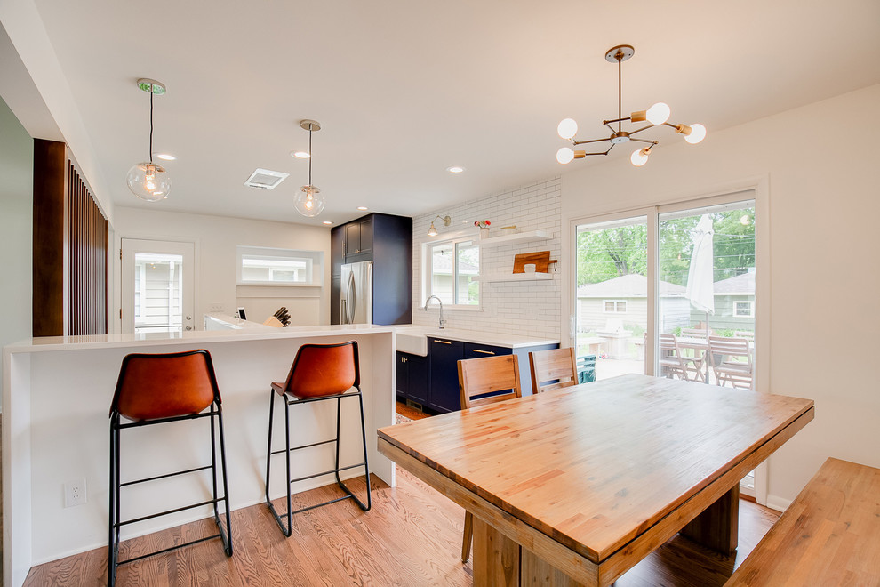 Photo of a mid-sized contemporary galley eat-in kitchen in Minneapolis with a farmhouse sink, shaker cabinets, blue cabinets, quartz benchtops, white splashback, subway tile splashback, stainless steel appliances, medium hardwood floors, no island and brown floor.