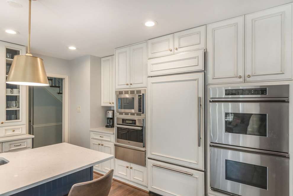 Transitional medium tone wood floor and brown floor kitchen photo in DC Metro with an undermount sink, recessed-panel cabinets, white cabinets, granite countertops, white backsplash, subway tile backsplash, stainless steel appliances, an island and white countertops