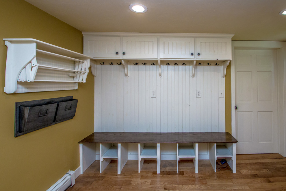 This is an example of a small country mudroom in Portland Maine with yellow walls, light hardwood floors, a single front door, a blue front door and brown floor.