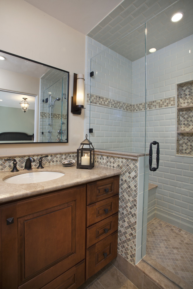Photo of a mid-sized traditional bathroom in San Francisco with raised-panel cabinets, medium wood cabinets, an alcove shower, beige tile, brown tile, gray tile, white tile, beige walls, porcelain floors, an undermount sink, porcelain tile, limestone benchtops, beige floor and a hinged shower door.