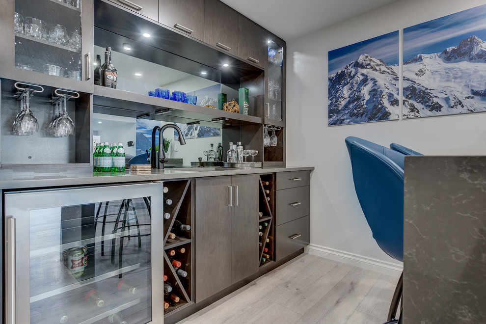 This is an example of a small contemporary galley wet bar in Calgary with an undermount sink, flat-panel cabinets, brown cabinets, quartz benchtops, grey splashback, glass sheet splashback, vinyl floors, grey floor and brown benchtop.