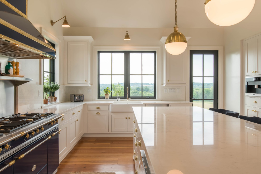 This is an example of a country u-shaped eat-in kitchen in Baltimore with a farmhouse sink, white cabinets, white splashback, coloured appliances, medium hardwood floors, with island, brown floor, white benchtop and vaulted.