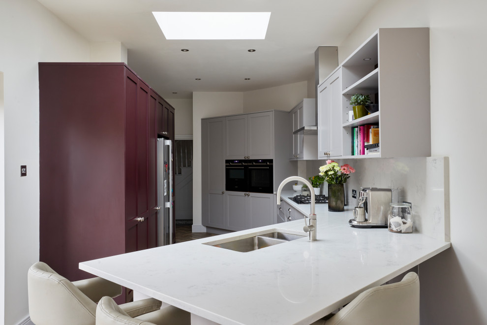 This is an example of a mid-sized traditional galley eat-in kitchen in London with shaker cabinets, grey cabinets, quartzite benchtops, white splashback, engineered quartz splashback, stainless steel appliances, medium hardwood floors, with island, brown floor and white benchtop.