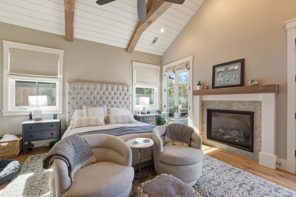 Photo of a large country master bedroom in San Francisco with beige walls, medium hardwood floors, a standard fireplace, a tile fireplace surround, brown floor, exposed beam, timber and vaulted.