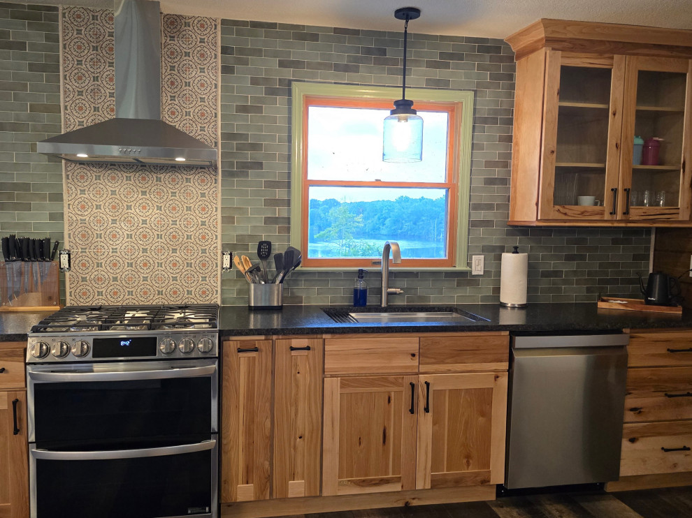 Example of a transitional dark wood floor kitchen design with an undermount sink, light wood cabinets, solid surface countertops, green backsplash and stainless steel appliances