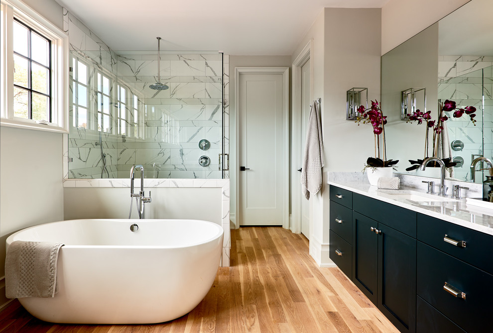 Design ideas for a transitional master bathroom in Charlotte with shaker cabinets, black cabinets, a freestanding tub, a corner shower, black and white tile, grey walls, light hardwood floors, an undermount sink, beige floor and a hinged shower door.