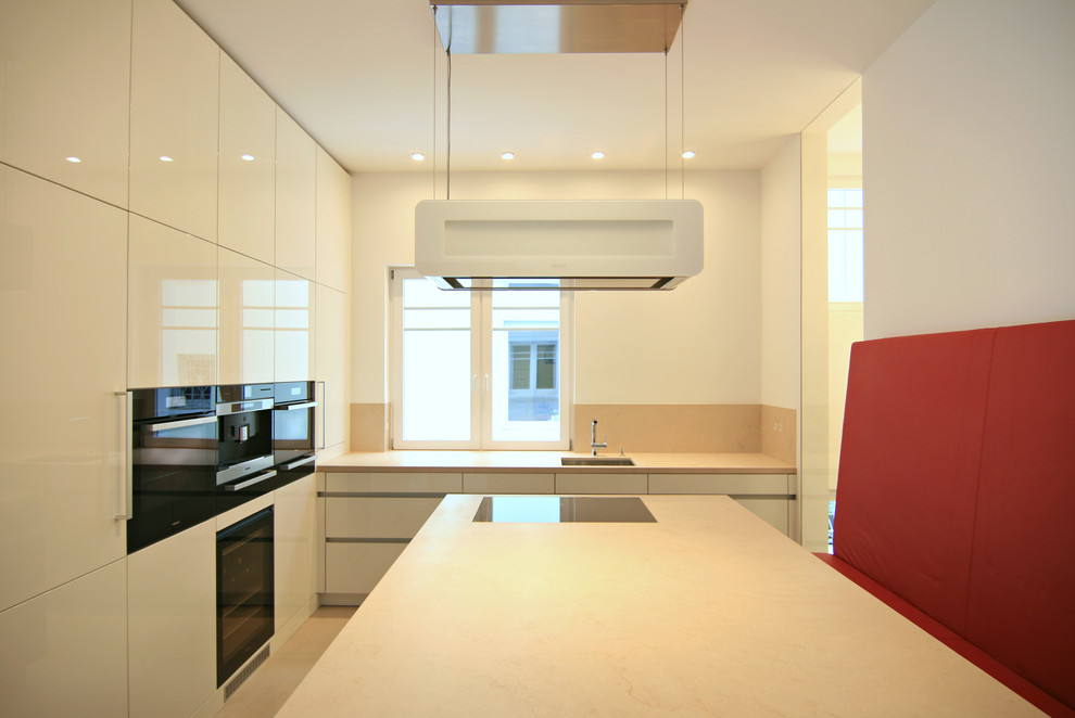 Photo of a mid-sized contemporary separate kitchen in Frankfurt with an undermount sink, flat-panel cabinets, white cabinets, limestone benchtops, beige splashback, stone tile splashback, black appliances and with island.