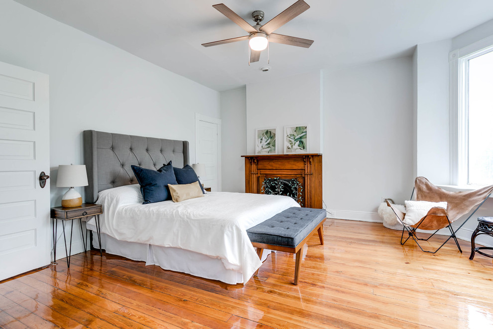 This is an example of a large transitional master bedroom in Wilmington with grey walls, light hardwood floors, a standard fireplace, a wood fireplace surround and brown floor.