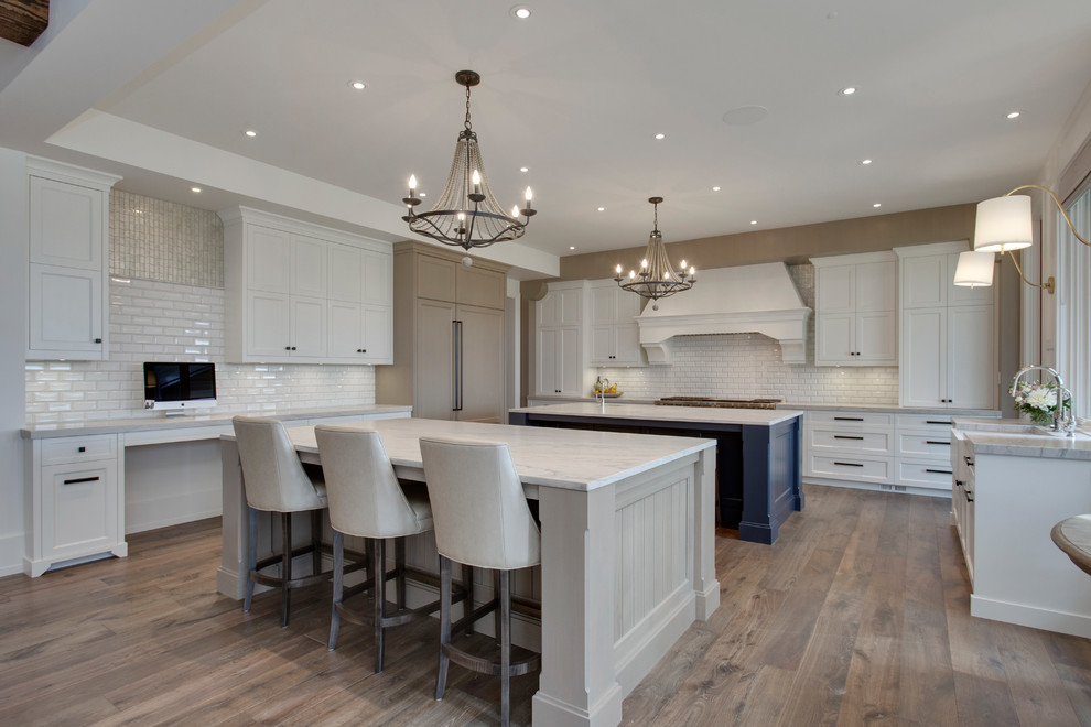 Inspiration for a large transitional u-shaped medium tone wood floor and brown floor kitchen remodel in Calgary with an undermount sink, louvered cabinets, white cabinets, granite countertops, white backsplash, two islands and white countertops