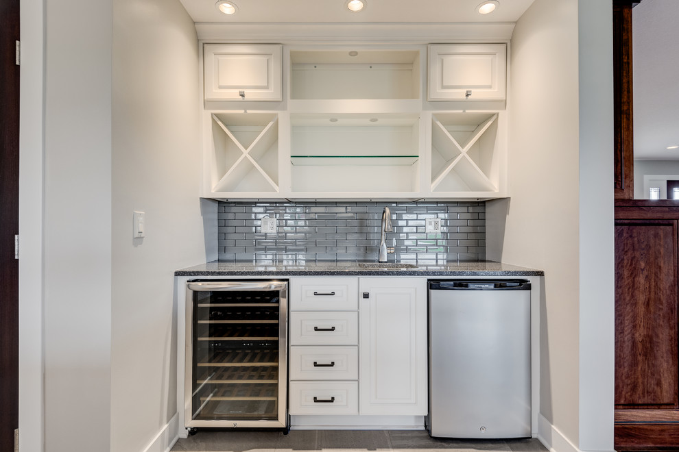 Design ideas for a mid-sized transitional u-shaped home bar in Chicago with raised-panel cabinets, white cabinets, quartzite benchtops, grey splashback, glass tile splashback, ceramic floors and beige floor.