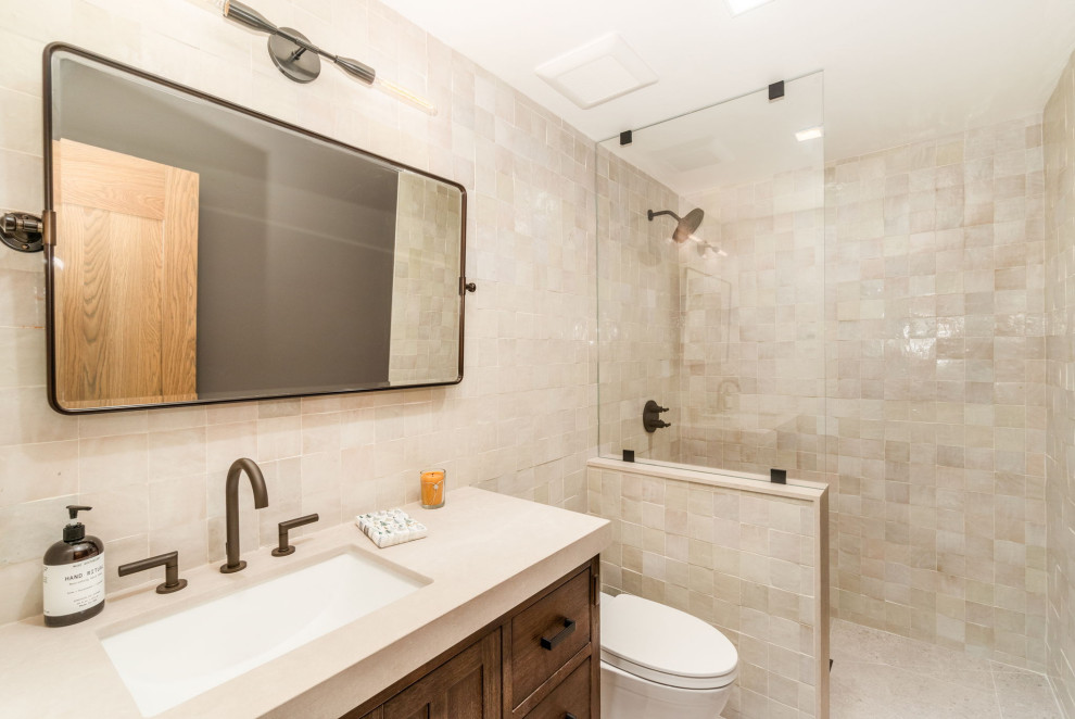 Inspiration for a mid-sized contemporary bathroom in Other with furniture-like cabinets, brown cabinets, a curbless shower, a one-piece toilet, beige tile, ceramic tile, beige walls, ceramic floors, an undermount sink, engineered quartz benchtops, beige floor, an open shower, beige benchtops, a single vanity and a freestanding vanity.
