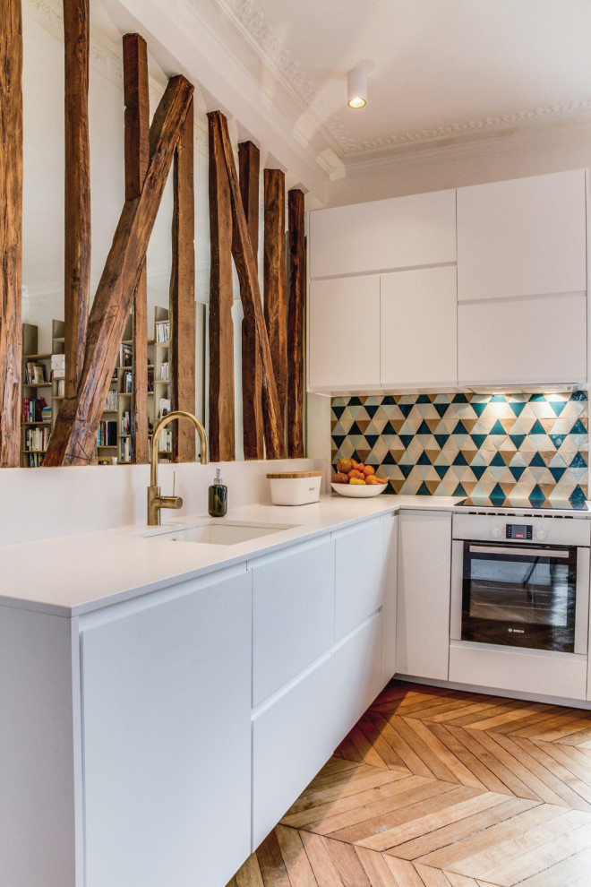 Photo of a mid-sized contemporary single-wall open plan kitchen in Paris with an undermount sink, flat-panel cabinets, white cabinets, multi-coloured splashback, terra-cotta splashback, panelled appliances, light hardwood floors, no island, brown floor and white benchtop.
