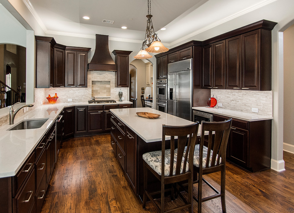 Inspiration for a large transitional u-shaped medium tone wood floor and brown floor open concept kitchen remodel in Dallas with a double-bowl sink, raised-panel cabinets, dark wood cabinets, quartz countertops, beige backsplash, mosaic tile backsplash, stainless steel appliances and an island
