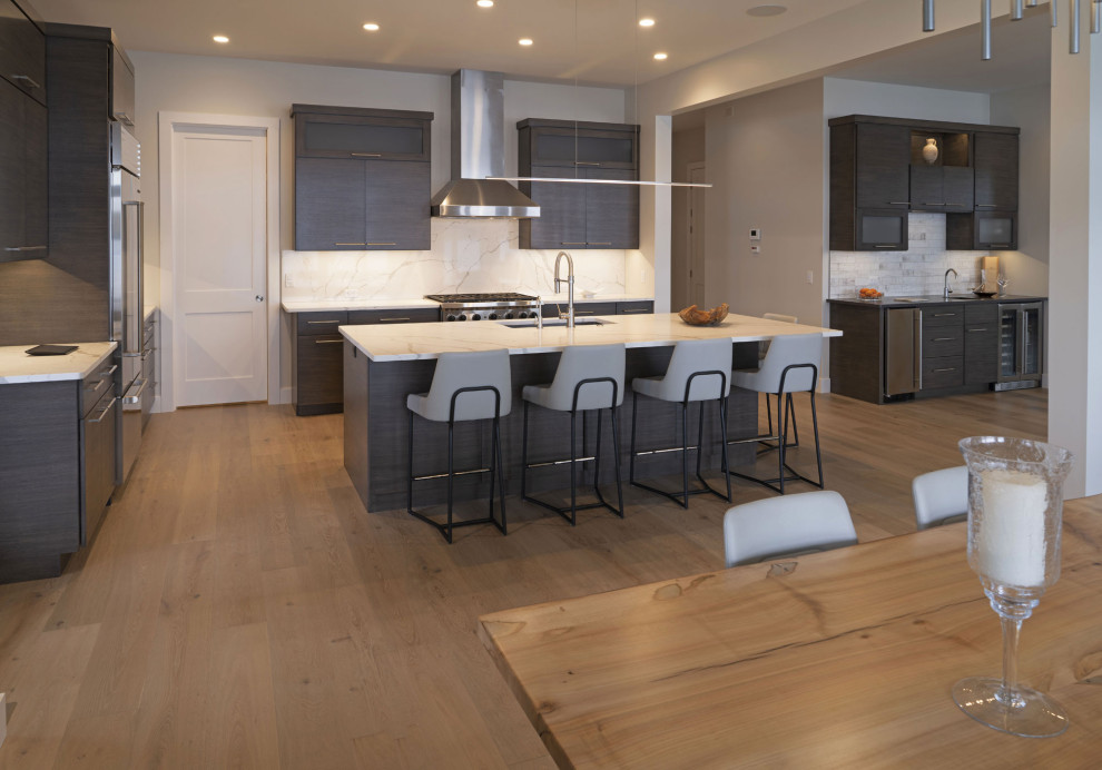 Large transitional l-shaped light wood floor and brown floor open concept kitchen photo in Other with an undermount sink, flat-panel cabinets, dark wood cabinets, quartz countertops, white backsplash, quartz backsplash, stainless steel appliances, an island and white countertops