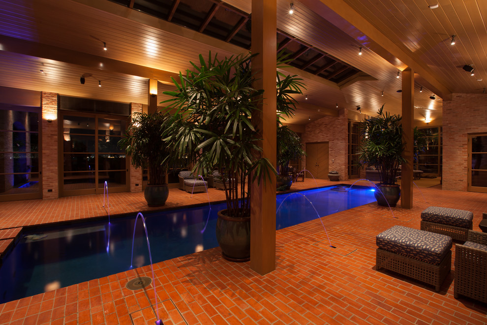 This is an example of a large traditional indoor rectangular pool in Austin with a water feature and brick pavers.