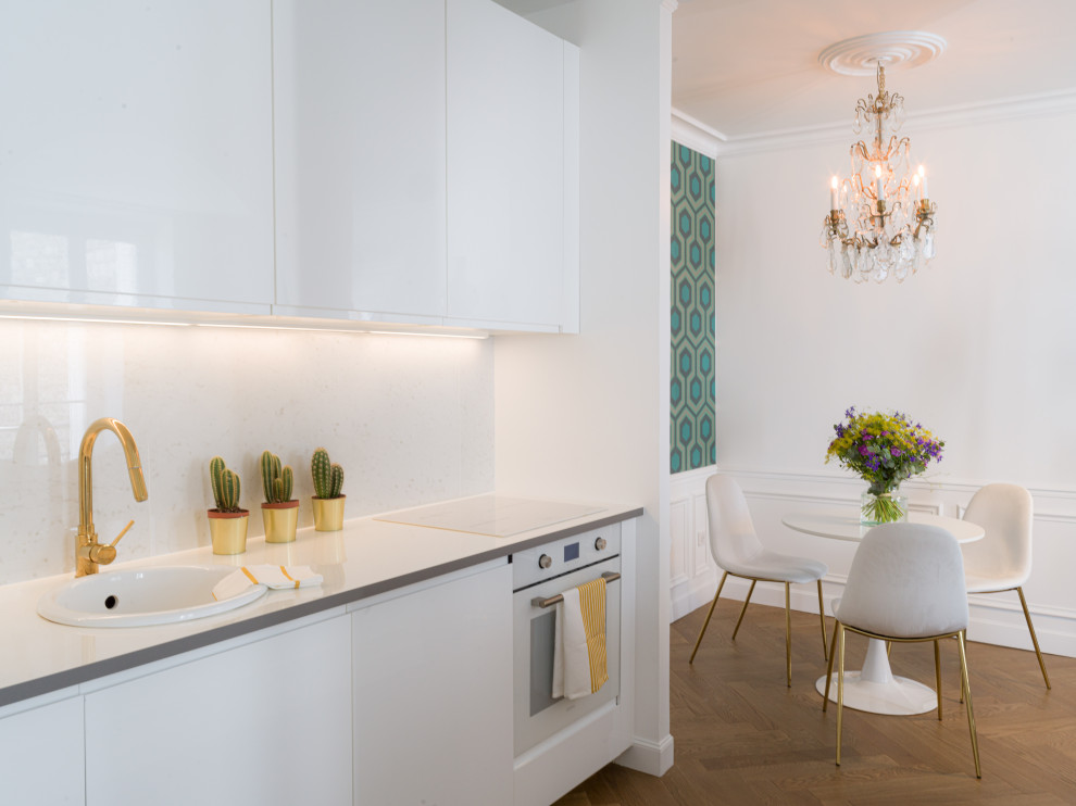 Photo of a mid-sized transitional single-wall open plan kitchen in Paris with a single-bowl sink, flat-panel cabinets, white cabinets, laminate benchtops, white splashback, marble splashback, white appliances, light hardwood floors, brown floor and white benchtop.