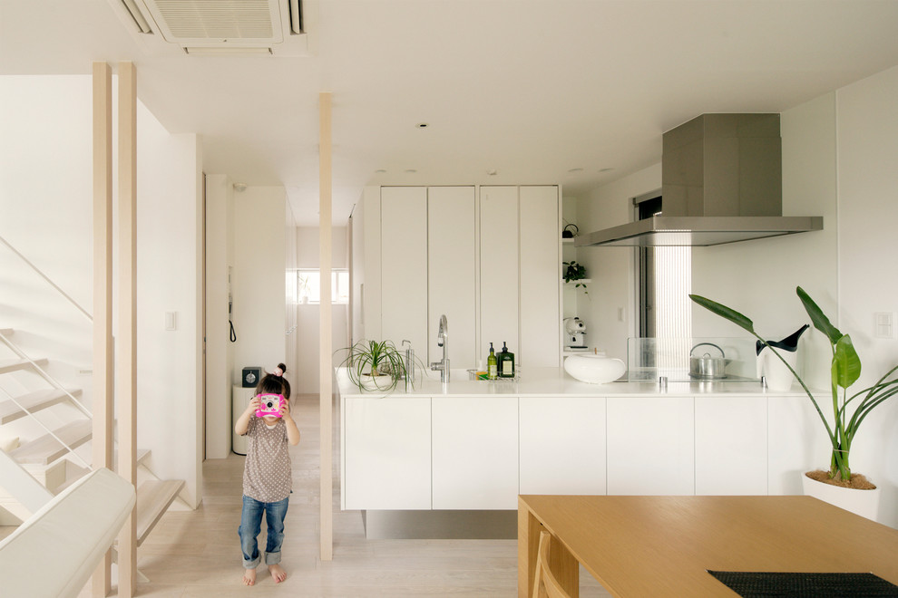 This is an example of a contemporary galley open plan kitchen in Nagoya with flat-panel cabinets, white cabinets, light hardwood floors, a peninsula, an integrated sink, white splashback, stainless steel appliances and beige floor.
