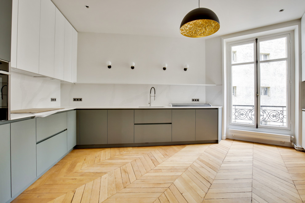 This is an example of a large transitional l-shaped separate kitchen in Paris with beaded inset cabinets, green cabinets, solid surface benchtops, white splashback, marble splashback, light hardwood floors, no island, brown floor and white benchtop.
