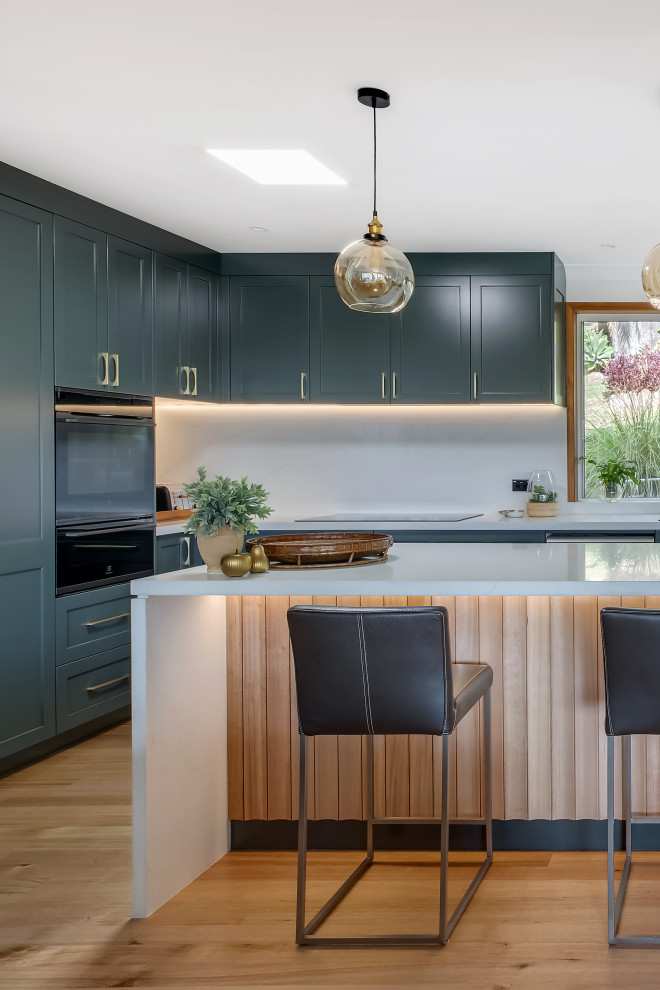 Example of a large transitional l-shaped medium tone wood floor and multicolored floor eat-in kitchen design in Sydney with a drop-in sink, shaker cabinets, green cabinets, quartz countertops, white backsplash, quartz backsplash, black appliances, an island and white countertops