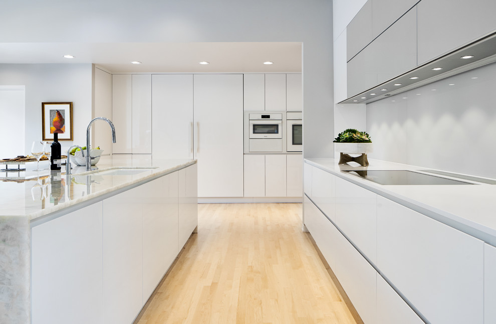 Photo of a large contemporary l-shaped eat-in kitchen in Dallas with an undermount sink, flat-panel cabinets, white cabinets, onyx benchtops, white splashback, glass sheet splashback, white appliances, light hardwood floors, with island, beige floor, beige benchtop and vaulted.