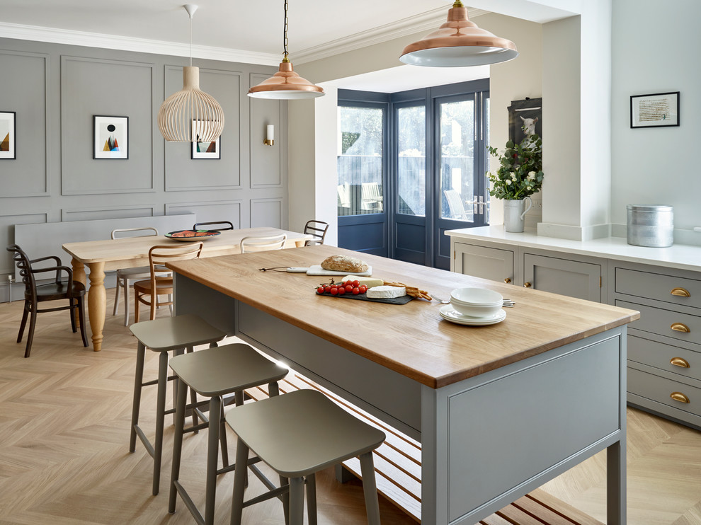 Transitional l-shaped eat-in kitchen in London with a farmhouse sink, shaker cabinets, grey cabinets, light hardwood floors and with island.