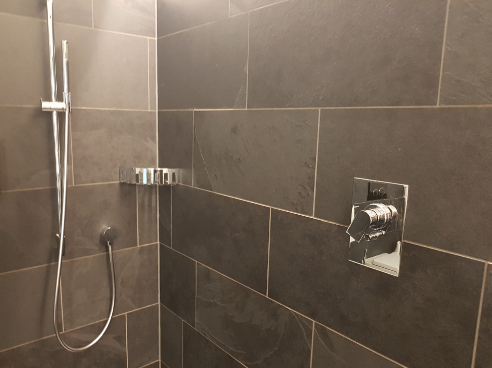 Foto på ett mellanstort funkis grå badrum med dusch, med öppna hyllor, grå skåp, en kantlös dusch, en toalettstol med separat cisternkåpa, grå kakel, skifferkakel, grå väggar, skiffergolv, ett fristående handfat, bänkskiva i glas, grått golv och med dusch som är öppen