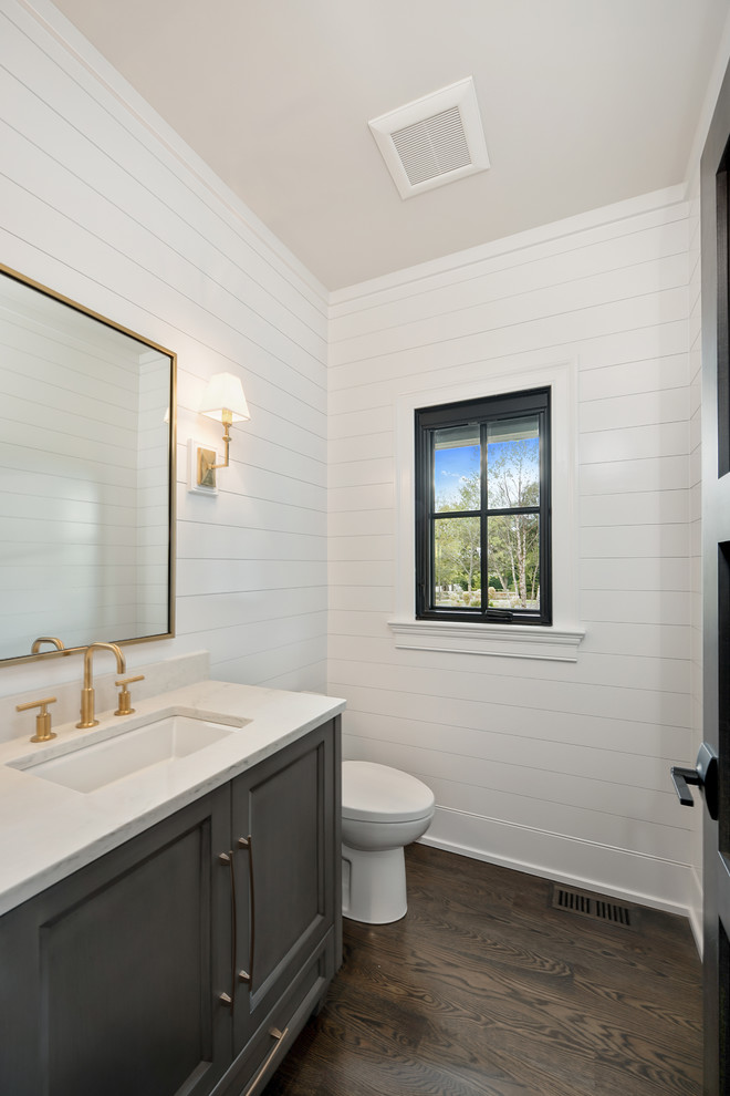 Inspiration for a mid-sized transitional powder room in Chicago with recessed-panel cabinets, grey cabinets, white walls, dark hardwood floors, an undermount sink, onyx benchtops, brown floor and white benchtops.