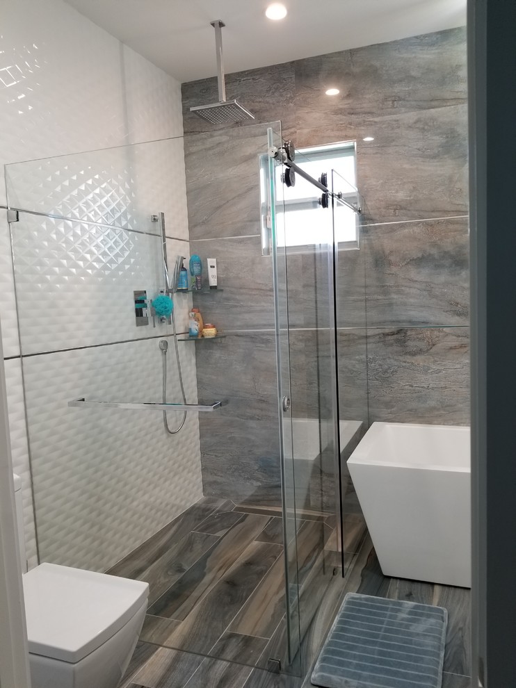 This is an example of a large modern kids bathroom in Miami with flat-panel cabinets, white cabinets, a freestanding tub, a curbless shower, a one-piece toilet, white tile, porcelain tile, white walls, porcelain floors, a wall-mount sink, engineered quartz benchtops, multi-coloured floor and a sliding shower screen.