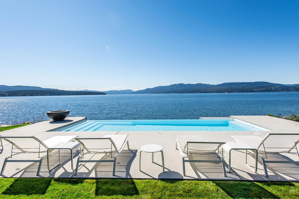 Design ideas for a large modern backyard rectangular infinity pool in Vancouver with concrete slab.