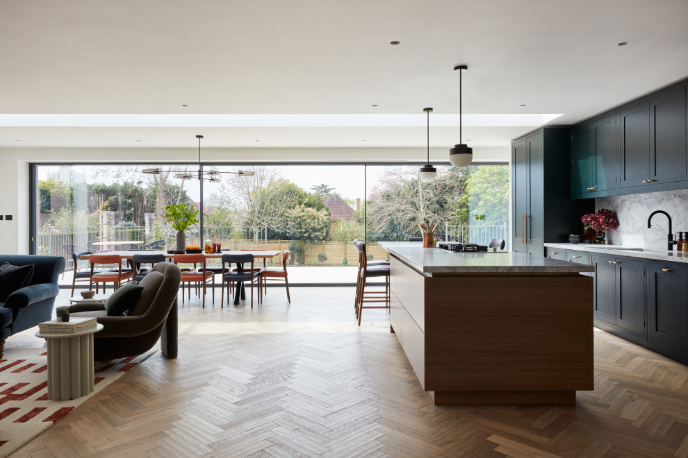 Photo of an expansive contemporary open plan kitchen in London with shaker cabinets, green cabinets, granite benchtops, grey splashback, granite splashback, medium hardwood floors, with island and grey benchtop.