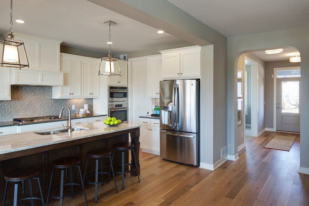 Kitchen - transitional light wood floor kitchen idea in Minneapolis with a double-bowl sink, white cabinets, quartzite countertops, gray backsplash, ceramic backsplash, stainless steel appliances and an island