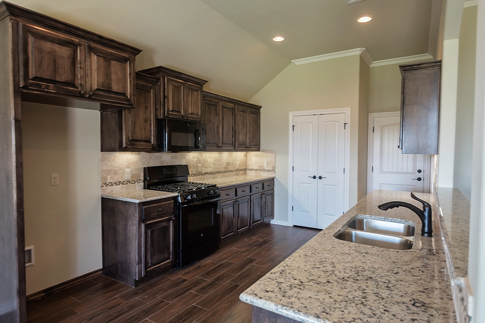 Mid-sized transitional galley eat-in kitchen in Oklahoma City with a double-bowl sink, raised-panel cabinets, dark wood cabinets, granite benchtops, beige splashback, porcelain splashback, black appliances, medium hardwood floors and brown floor.